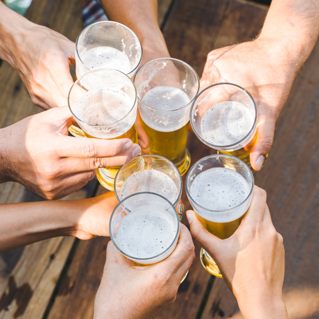 The hands of six people toasting draft beer in glasses