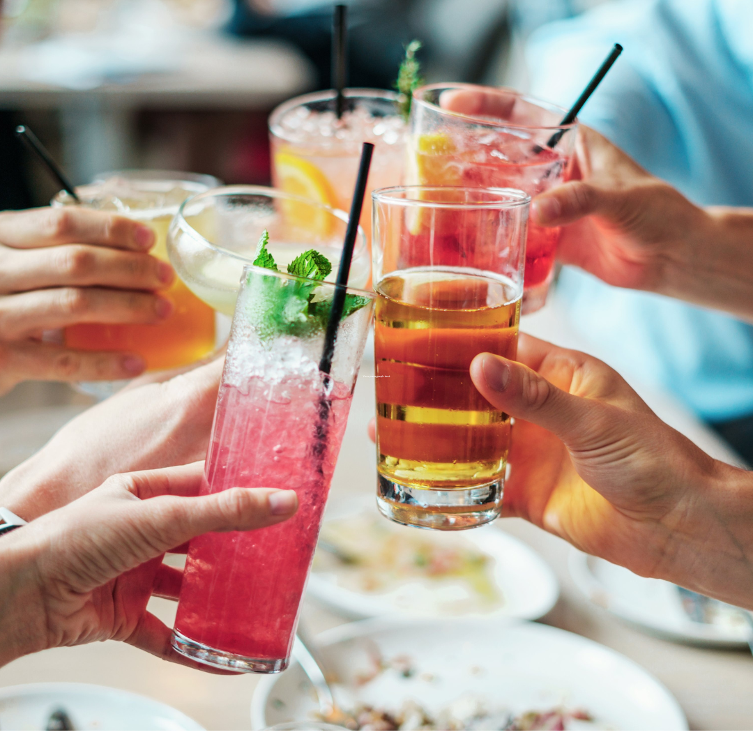 The hands of six people toasting with a variety of cocktails in different glasses