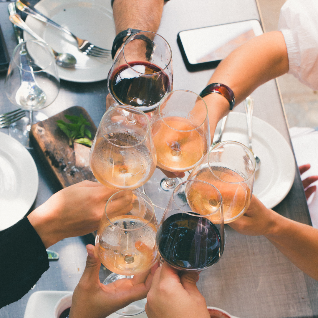 Five people sitting at a dinner table toasting wine in glasses