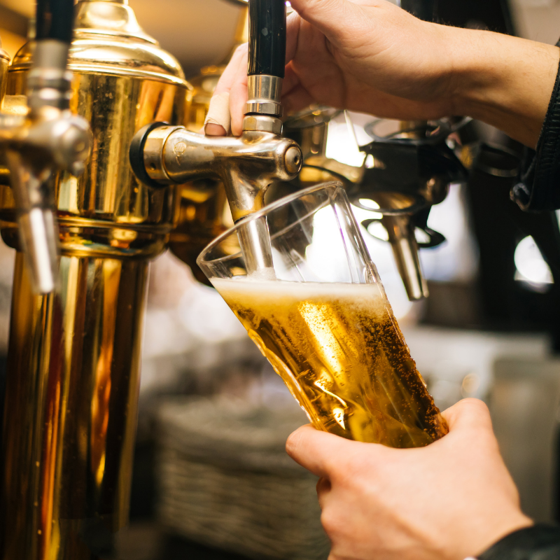 Person pouring a draft beer into a glass from a gold beer tap