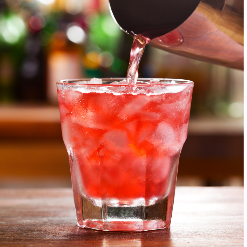 Pinkish red cocktail being poured from a cocktail shaker into a rocks glass